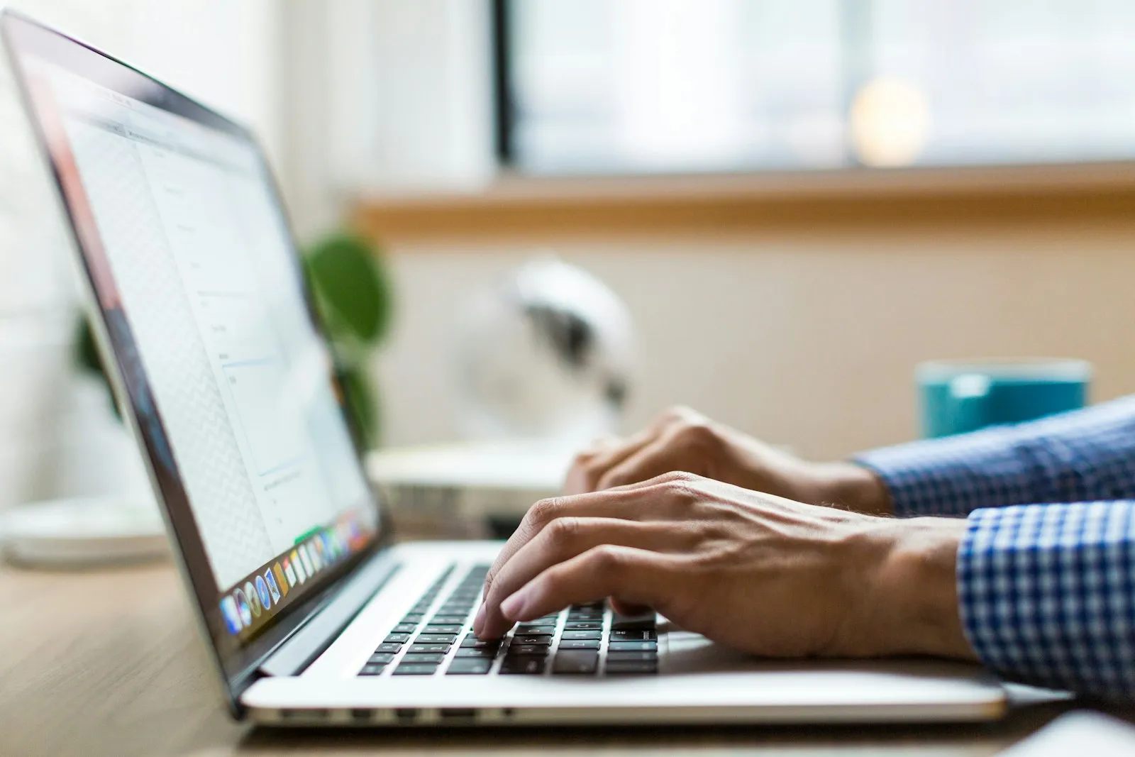 A person typing on a laptop at a bright desk