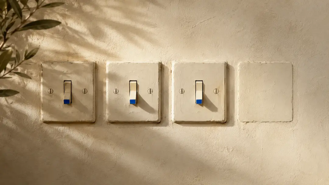 Four old-fashioned light switches on a sunlit plaster wall. Three are real switches flipped down to the off position; the fourth plate is blank and sealed over, with no switch on it at all