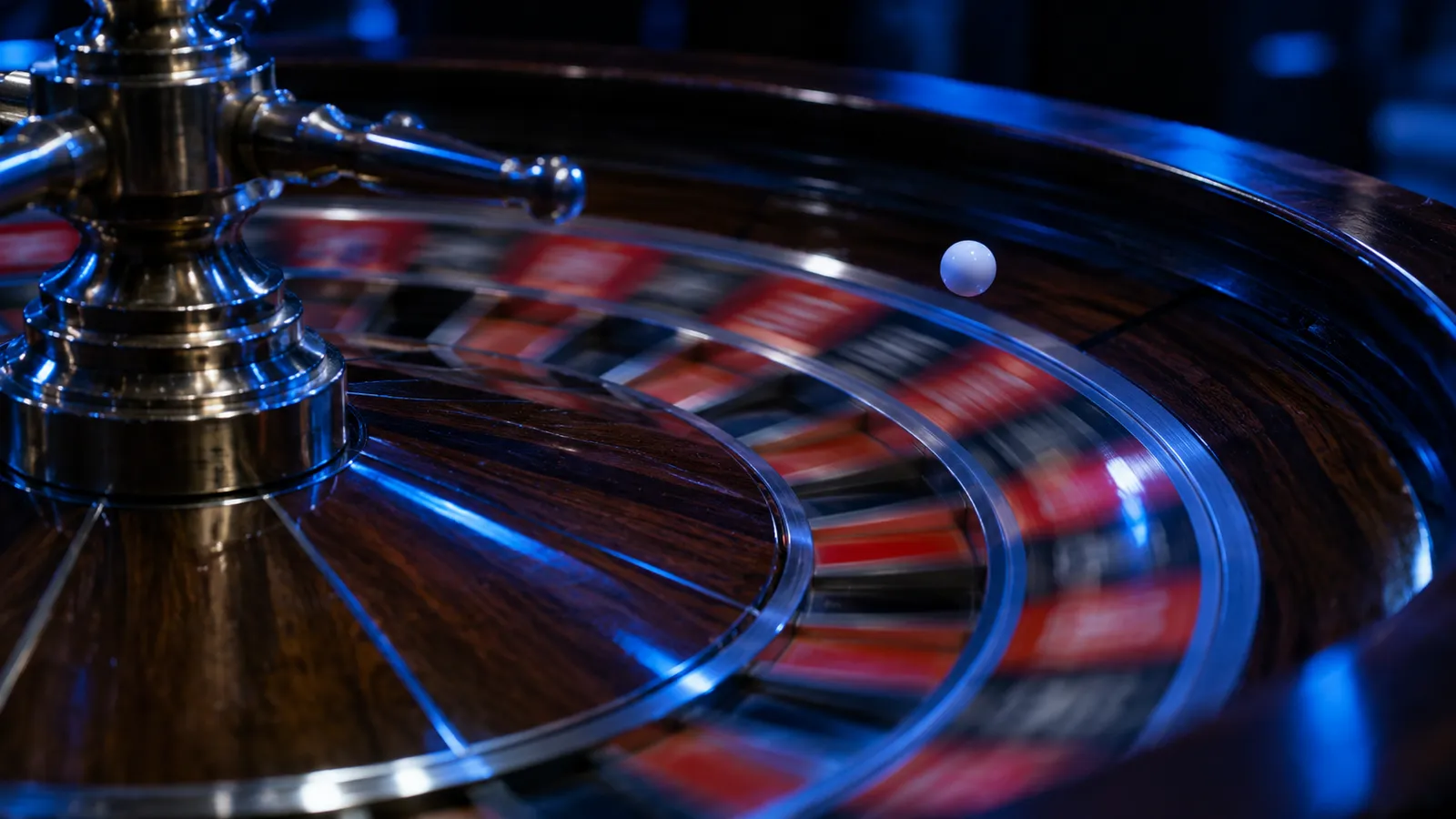 A casino roulette wheel lit in blue, the white ball mid-bounce on the spinning numbered track